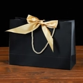 Elegant black matte paper gift bag featuring a large golden satin bow and braided handles - 19x15x7cm / Black