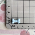 Mini light blue bone-shaped resin accessory measured at 1.8cm on a grid ruler - Blue