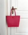 Détail du grand sac cabas tressé rouge rose suspendu à une porte en bois blanc - Rouge