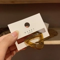 Bernsteinbraune Dreieck-Haarklammer auf Markenkarte vor einem Hintergrund aus Holzregalen - Kaffeebraun