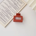 Detail einer minimalistischen quadratischen Haarklammer in Mattbraun auf offenem Buch - Matt Orange
