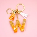 Detail of a letter W resin keychain with orange corn kernels, gold foil, and dual tassels - Letter W