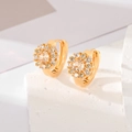 Makroaufnahme goldener Blumenohrringe mit Zirkonia auf texturiertem Naturstein - Champagner