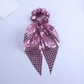 Close-up of pink sequined scrunchie with long ribbon featuring square sparkling patterns - Pink