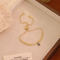 Dettaglio del bracciale a sfere dorato regolabile con occhio blu e ciondolo J - Lettera J