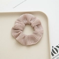 Detail showing champagne pleated fabric scrunchie with glossy texture on beige tray - Pink