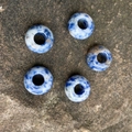 Five natural blue and white stone abacus beads with large holes on dark rock surface - Blue Spot Jasper