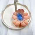 Matte peach pink plumeria flower claw clip with blue gradient center on a display stand - Korean Pink (Rubber Paint Lucky Flower)
