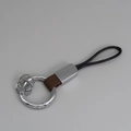 Porte-clés en cuir marron avec anneaux métalliques et corde noire sur fond gris - Marron + Argent