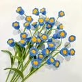 Close-up of handmade blue crochet lily of the valley flowers with green leaves - Blue