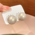 Primer plano de grandes pendientes de perlas crema exhibidos en una tarjeta blanca - Champán