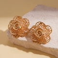 Macro shot of gold double-layer hollow rose stud earrings on a textured stone base - Gold / Gold