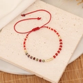 Handcrafted red woven bracelet with gold metal beads on a natural stone surface - Red Marble / Red