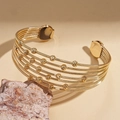 Detail der goldene mehrlagige Armspange mit Spiralkugeln auf einem Naturstein - Gold