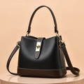Minimalist black and brown bucket bag with gold hardware shown on a round pedestal - Black