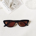 Detail of vintage cat-eye sunglasses with black frame and amber lenses on textured white background - Black Brown