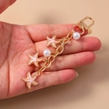 Gold keychain featuring pink starfish charms and white pearls held in palm - Starfish Style / Pink Starfish