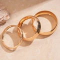 Detailed view of three polished gold metal bangles in varying widths on a stone surface - Gold (3-Piece Set)