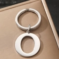 Silver metal keychain with 'O' letter pendant on a textured box lid for gifting - Letter O