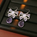 Gros plan de boucles d'oreilles nœud avec gemmes violettes et cristaux de luxe - Crochets d'Oreilles Violets