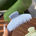 Close-up of light blue marble textured acetate claw clip held against a natural plant background - Jelly Blue - 7 Teeth Claw