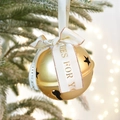 Goldene Weihnachtsglocke mit Sternenausschnitten und weißem Band an einem verschneiten Zweig - Goldene Glocke mit Band