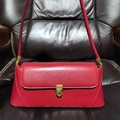 Sac baguette chic en cuir rouge avec fermoir doré sur un canapé en cuir sombre - Rouge
