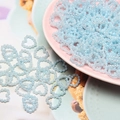 Macro shot of light blue heart-shaped ABS pearls spilling from a small pink bowl - Blue