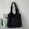 Detailed view of black canvas tote bag with large front pocket against a white wall - Black