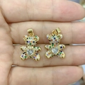 Close-up of golden teddy bear pendant with colorful stones and heart-shaped gem in hand - Colorful