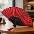 Classic red fabric folding fan with black plum blossom pattern and tassel on wooden table - Style 36 (Red Plum Joy Fan) (New Style)