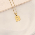 Collana dorata con ciondolo lettera B e trama a nido d'ape su piatto di ceramica bianca - Lettera B