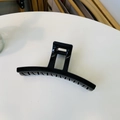 Close-up of a large black glossy hair claw clip showing a metal spring on a white table - Glossy Black