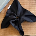 Dettaglio di un grande elastico a fiocco in raso nero con texture setosa su legno - Nero