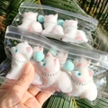 Close-up of white plush cat keychains with silver chains in clear packaging - Queue Kittens