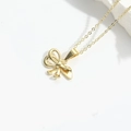 Close-up of golden bow pendant with cross chain on a minimalist white stone background - Knot (Gold)