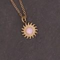 Primo piano del ciondolo a girasole dorato con gemma rosa su sfondo di pietra - Sole Rosa