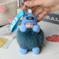 Close-up of fluffy fox fur ball keychain with sleeping baby doll and blue knitted hat - Light Green