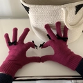 Close-up of pink knitted gloves with black bows shown in a heart shape gesture - One Size / Purple