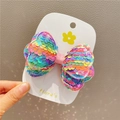 Detail of sequined rainbow bow hair clip with gradient glitter effect on a card - Rainbow