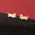 Vista macro de pendientes de gato minimalistas en acero inoxidable dorado sobre textura - Silueta de Gato Caminando (Oro Rosa 790)