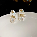Detalle macro de pendientes ovalados de nácar con mariposa de oro y gemas - Pin de Plata-Oro-Blanco