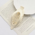 Beige oval hair claw clip for women displayed on vintage book page with white plates - Bright White