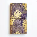 Travel journal featuring purple and yellow tropical monstera leaf patterns and black elastic band - Abundant Flowers