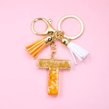 Detail of letter T resin keychain with gold foil flakes and orange tassel charms - Letter T