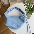 Dettaglio borsa a tracolla in nylon azzurro con tracolla arricciata su un tavolo bianco - Blu