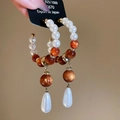 Makro-Detail von Tropfenohrringen mit weißen Perlen und orangen Perlen an Silberstiften - Perlen-Tropfen-Stil / Weiß & Bernstein