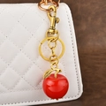 Red apple keychain with golden hardware charm on a white quilted handbag - Solid Red