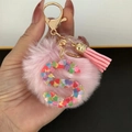 Detail of pink faux fur pom pom and resin letter S keychain with colorful heart glitter - Letter S