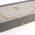 Detail of golden stainless steel letter K pendant necklace on grey velvet display tray - Letter K / Gold